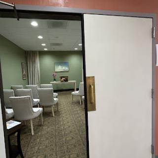 An open door revealing a softly lit meeting room with white chairs arranged in rows.