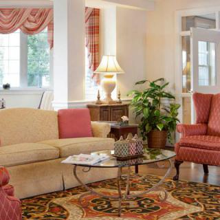 A cozy living room with a beige sofa, red armchairs, a glass coffee table, and decorative elements such as a lamp and an indoor plant.