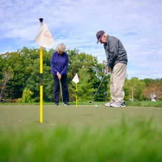 Two senior individuals enjoying a game of golf outdoors on a sunny day.
