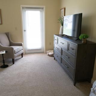 A cozy living room with a television, armchair, and dresser.