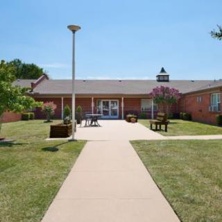 A brick building with a central pathway, surrounded by lawn and benches under a clear blue sky.