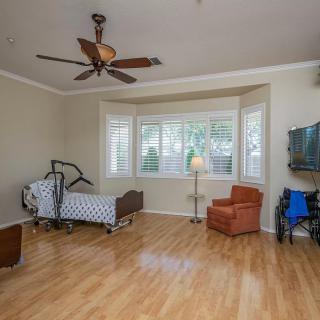 A spacious bedroom with a hospital bed, hardwood flooring, and a ceiling fan.