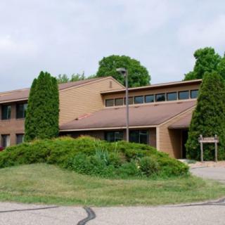 A two-story brick building surrounded by greenery under a cloudy sky.