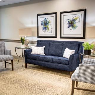 A modern living room with a blue sofa, patterned chairs, and framed artwork on the wall.