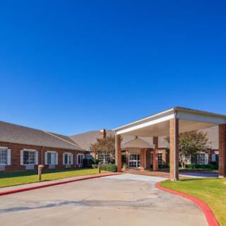 A view of a brick building with a covered entrance and driveway under a clear blue sky.