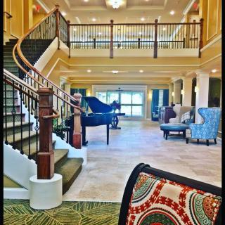 A spacious lobby featuring a grand piano, elegant staircase, and comfortable seating area.