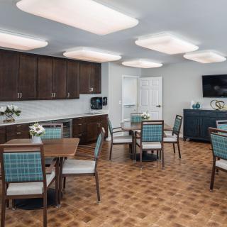 A modern dining area with wooden tables, upholstered chairs, and sleek kitchen cabinets.