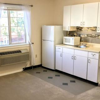A compact apartment kitchen with white cabinets, a fridge, and a microwave next to a window.