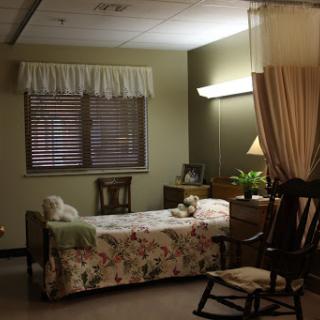 A cozy hospital room featuring a floral-patterned bed, comfortable furniture, and warm lighting.