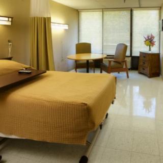 A clean and well-organized hospital room with a bed, chairs, and a table.