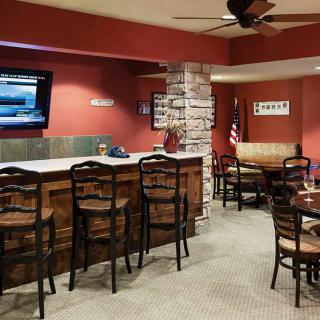 A cozy bar with wooden chairs, tables, and a television against a brick accent wall.