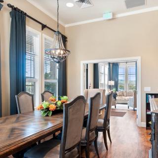 A well-furnished dining room with a large table, chairs, chandelier, and decorative flowers.