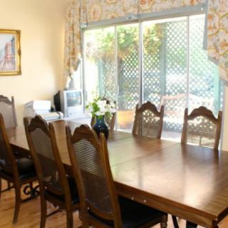A dining room with a large wooden table and chairs, featuring a bright window view.