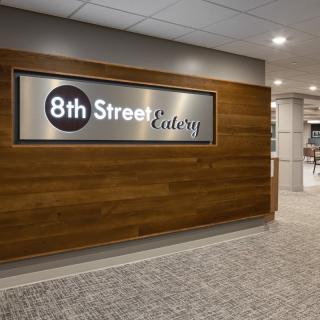 The entrance to the 8th Street Eatery features a modern sign on a wooden wall.