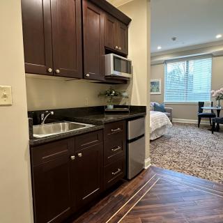 A cozy studio apartment featuring a kitchenette with wood cabinets, a sink, microwave, and mini fridge.