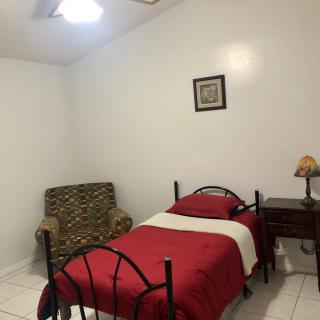 A simple bedroom with a single bed, red bedding, and a small nightstand.