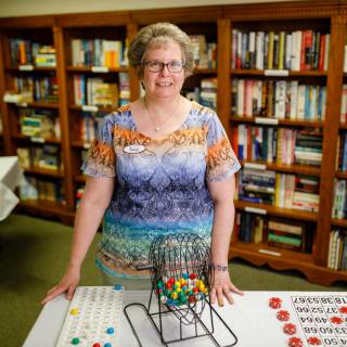 A person stands in front of bingo equipment in a library setting.