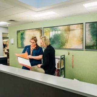 Two people discussing paperwork at a reception desk in an office.
