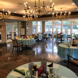 An elegant dining room set up for an event, featuring chandeliers and neatly arranged tables and chairs.