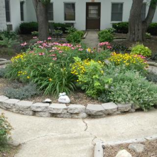 A vibrant garden filled with colorful flowers and lush greenery, surrounded by a stone border and a walking path.