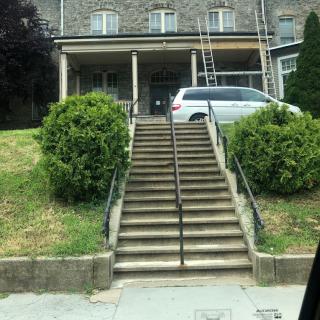 A house with a set of stairs leading up to it, flanked by bushes and a parked car.