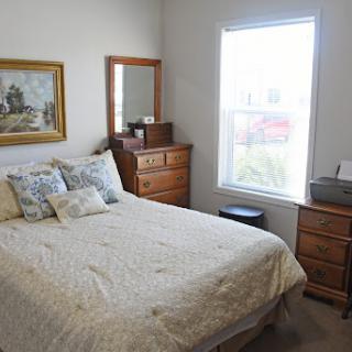 A cozy bedroom featuring a comfortable bed, wooden furniture, and bright natural light streaming through the window.