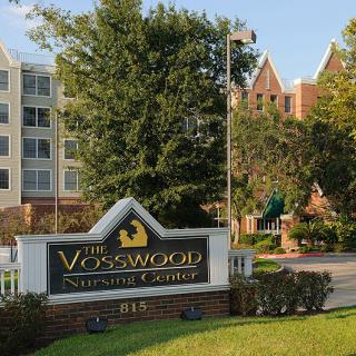 Entrance sign for The Vosswood Nursing Center with surrounding buildings and trees.