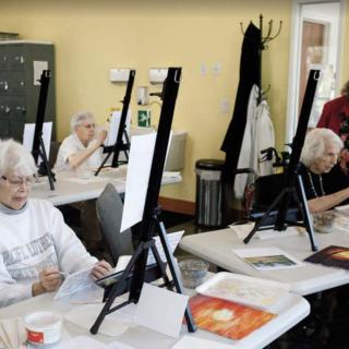 A group of seniors engaged in a painting class, working on their art pieces at easels.