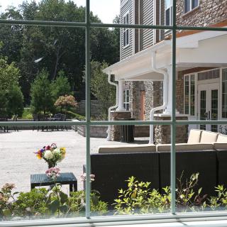 View through a window overlooking a patio with outdoor seating and flowers.
