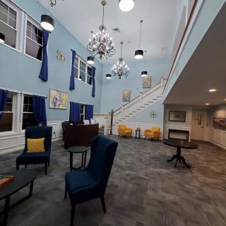A spacious lobby featuring elegant chandeliers, comfortable seating, and a staircase leading to an upper level.