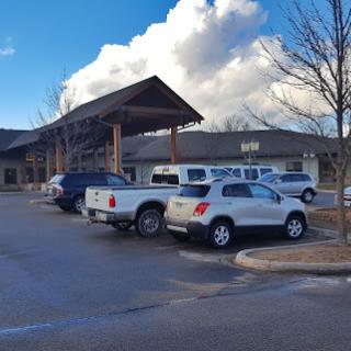 A view of a building with a parking lot filled with vehicles under a cloudy sky.