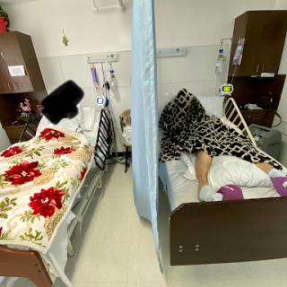 Two hospital beds with patients, separated by a privacy curtain.