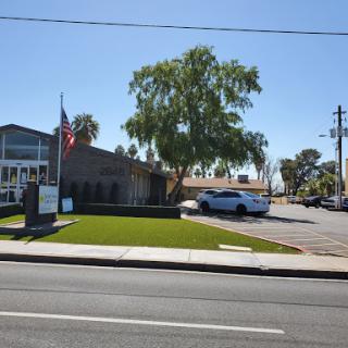 A view of a commercial building with a tree and flag in front, located on a sunny day.