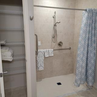 A bathroom with an open shower area, featuring a blue patterned shower curtain and grab bars. Towels are neatly arranged on nearby shelves.