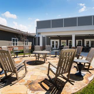 A sunny outdoor patio with rocking chairs arranged around a circular stone seating area.