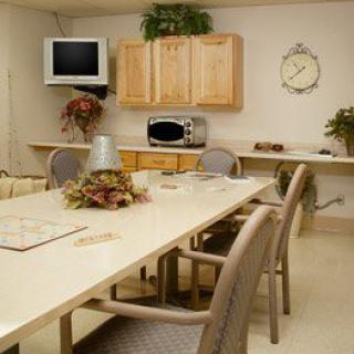 A well-arranged meeting room featuring a long conference table, chairs, a wall-mounted television, and basic kitchen amenities.