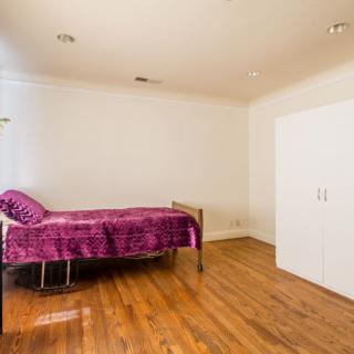 A minimalist bedroom with a single bed covered in purple bedding and a wooden floor.