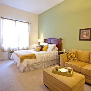 A cozy bedroom with a comfortable bed and a sofa, featuring warm colors and ample natural light.
