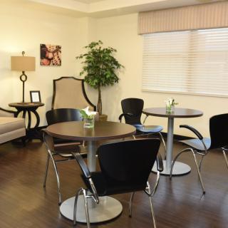 A comfortable waiting area with round tables, black chairs, a cozy sofa, and decor including a lamp, indoor plant, and wall art.