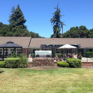 A cozy house with a spacious backyard and patio, featuring outdoor furniture and surrounded by a lush garden on a sunny day.