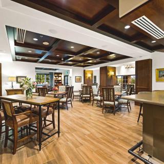 A spacious and well-lit dining area with wooden flooring, featuring multiple tables and chairs arranged neatly.