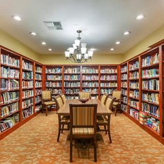 A cozy library reading room with bookshelves and a central table surrounded by chairs.