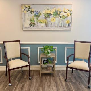 A serene waiting area featuring two elegant chairs and a decorative floral painting.