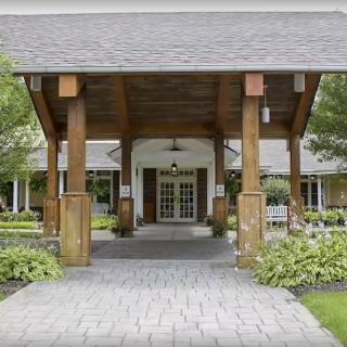 A covered entrance to a building featuring wooden pillars and landscaped surroundings.