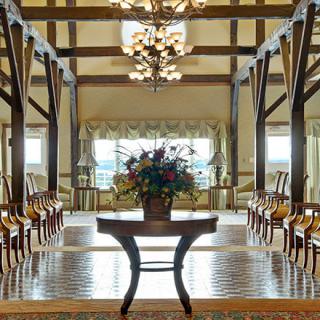 A beautifully decorated interior with wooden beams and chandeliers, featuring a central floral arrangement on a polished table.