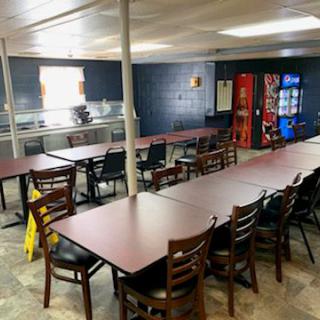 An empty break room with tables and chairs arranged, and vending machines in the corner.