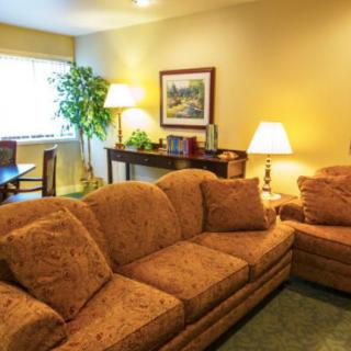 A cozy living room featuring a large couch, table lamps, framed artwork, and a potted plant.