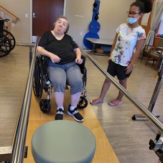 A wheelchair user participates in a physical therapy session with the support of a caregiver.