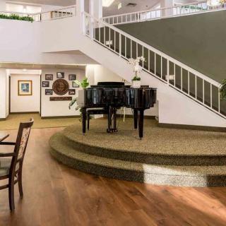 A spacious living room featuring a grand piano on a raised platform, with a staircase and artwork adorning the walls.