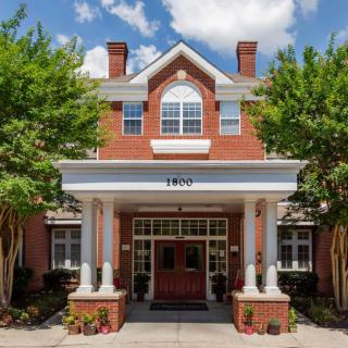 A brick building with an inviting entrance, framed by white columns and surrounded by trees.